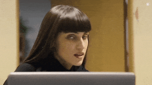 a woman with bangs is looking at a computer screen and making a funny face