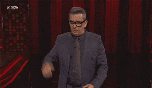 a man in a suit and tie stands in front of a red curtain with the words late motiv on the bottom