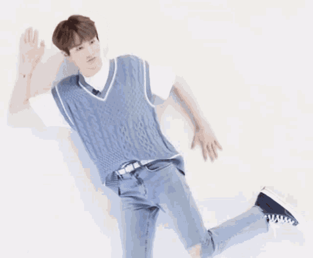 a young man is laying on the floor wearing a blue vest , jeans and a white t-shirt .