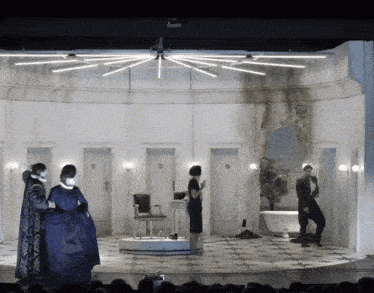 a group of people standing on a stage in front of a bathroom with a sign on the door that says ' a '