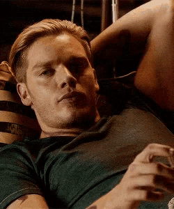 a man in a green shirt is laying on a couch with his arms crossed .