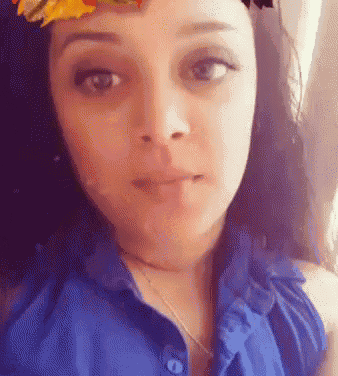 a woman wearing a blue shirt and a flower crown on her head is looking at the camera .