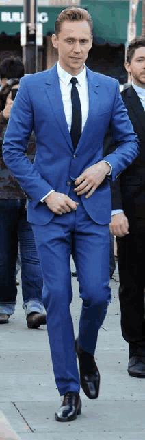 a man in a blue suit and tie walks down a street
