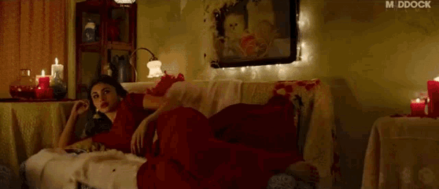 a woman in a red dress is laying on a couch in a room with candles and a picture on the wall .