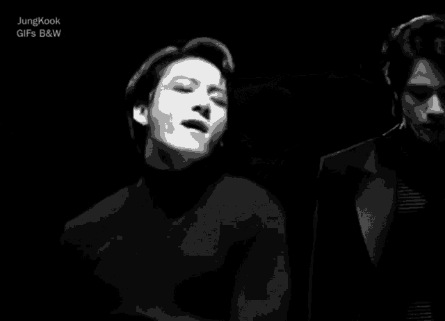 a man in a black turtleneck sweater is sitting in a dark room with his hands on his chest .