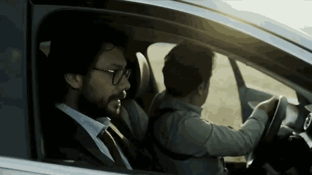 a man in a suit and tie is driving a car with another man in the back seat .