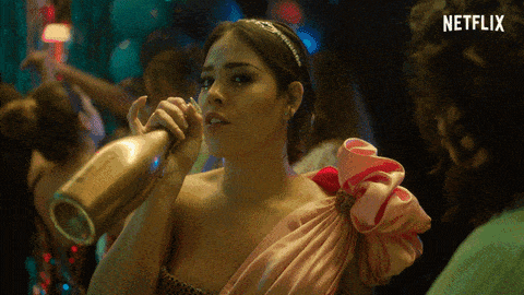 a woman in a pink dress is drinking from a bottle with a netflix logo behind her