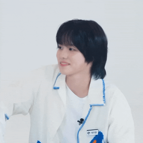 a young man with black hair is wearing a white jacket with a blue collar and a white shirt .
