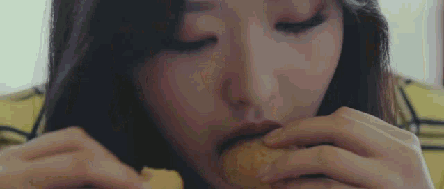 a close up of a woman eating a hamburger with her eyes closed .