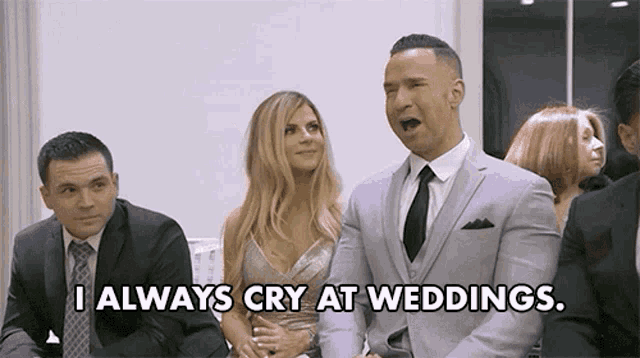 a man in a suit and tie is sitting next to a woman in a dress and saying i always cry at weddings .