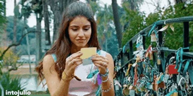 a woman is holding a piece of paper in front of a bridge with locks .