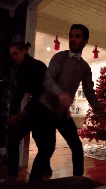 a man and woman are dancing in front of a red christmas tree