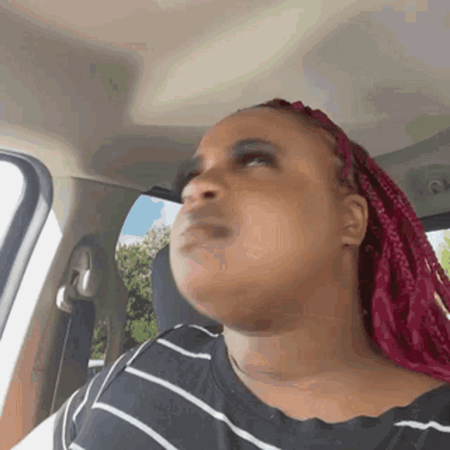 a woman with pink braids is sitting in a car looking out the window .