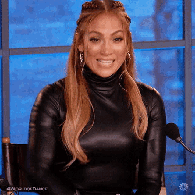 a woman is sitting in front of a microphone wearing a black turtleneck and smiling .
