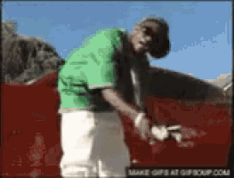 a man in a green shirt and white shorts is standing in front of a red car