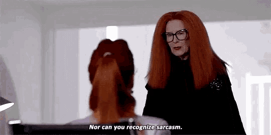 a woman with red hair and glasses is standing next to another woman and talking to her .