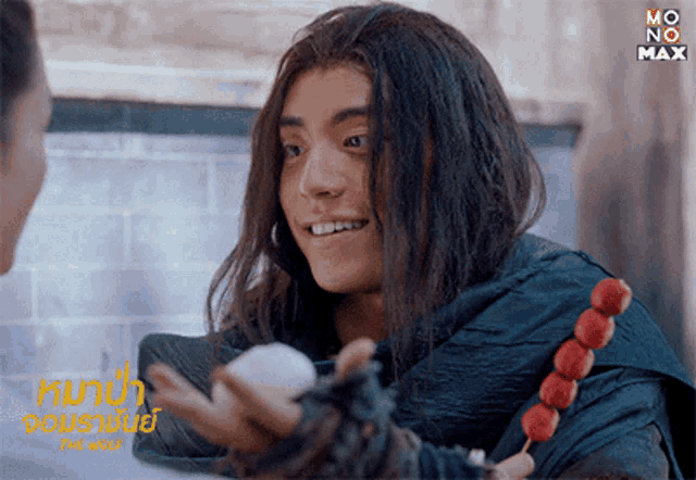 a man with long hair is smiling while holding something in his hand and the word max is on the bottom right