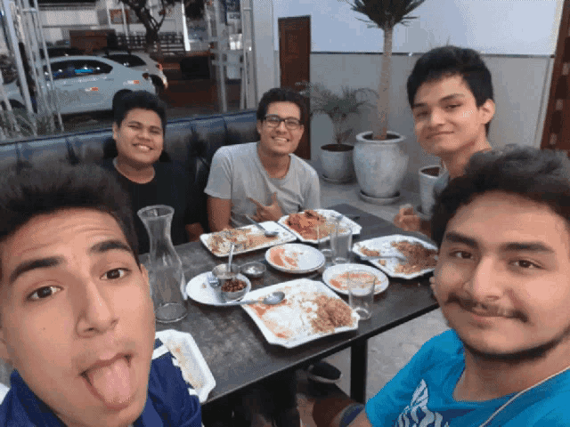 four young men are sitting at a table with plates of food