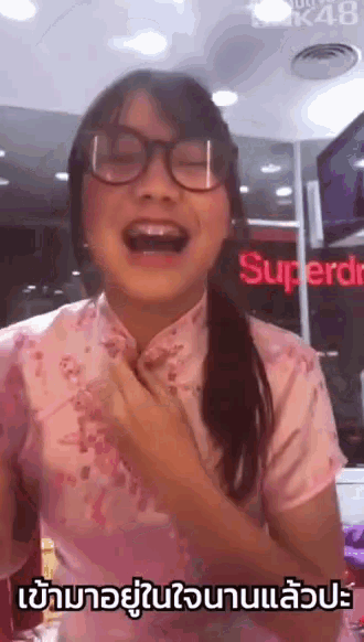a girl wearing glasses and a pink dress is laughing in front of a superdr sign