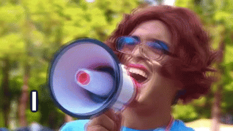 a woman wearing a wig and glasses is holding a megaphone in front of her mouth .