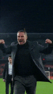 a man in a suit stands on a field with his arms in the air