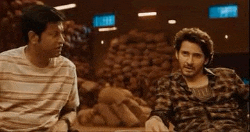 two men are sitting next to each other in front of a pile of vegetables .