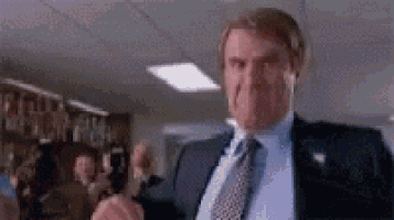 a man in a suit and tie is standing in a room with his hands in the air .
