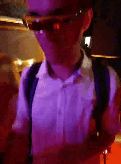 a man wearing sunglasses and a backpack stands in front of a purple light