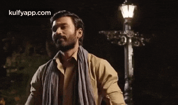 a man with a scarf around his neck is standing in front of a street light at night .