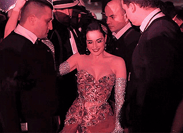 a woman in a dress and gloves is surrounded by men in suits