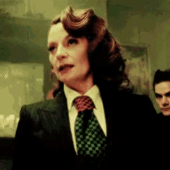 a woman in a suit and tie with a man in the background