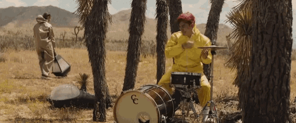 a man in a yellow suit sits on a drum set with the letter e on it