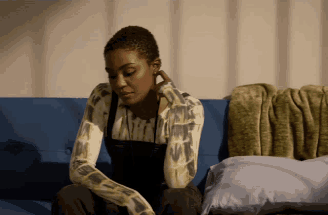 a woman sits on a blue couch with a pillow and a blanket