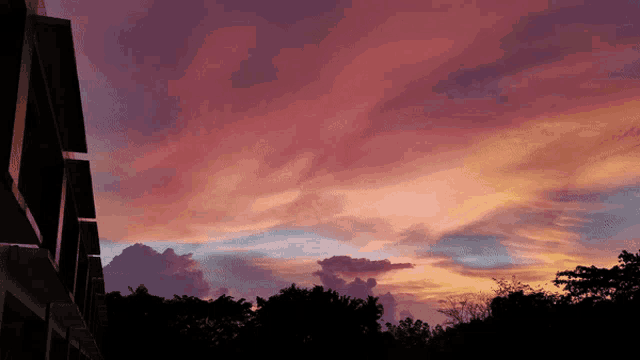 a building is silhouetted against a pink and purple sunset sky
