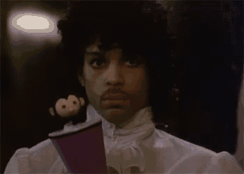 prince is holding a purple cup and a stuffed monkey in his hand .