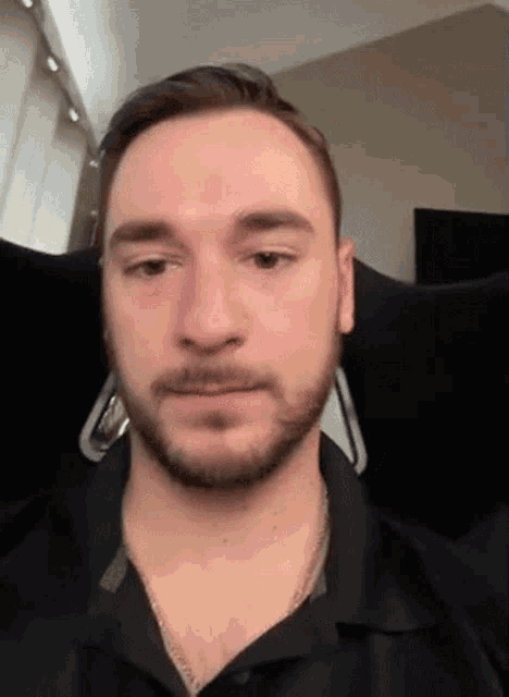 a man with a beard wearing a black shirt is looking at the camera .