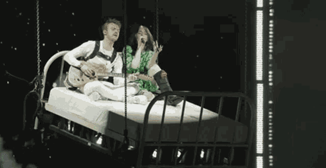 a man is playing a guitar while a woman sings on a bed