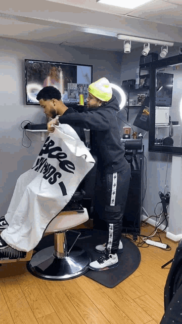 a man is getting his hair cut by a barber with a cape that says free minds on it