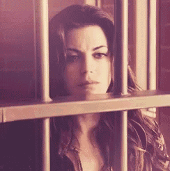a woman is behind bars in a jail cell looking out .