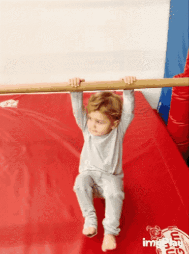 a little boy is hanging from a wooden bar on a red mat with a monkey on it