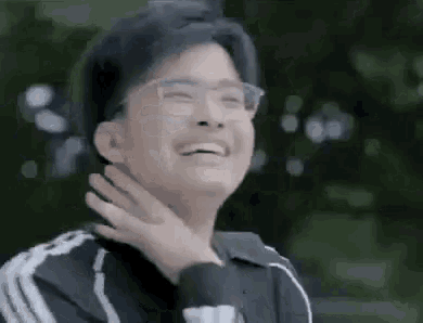 a young man wearing glasses is laughing while holding his hand to his chin .