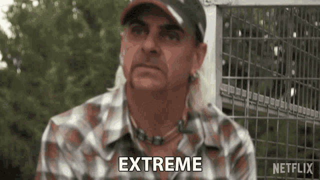 a man in a plaid shirt and hat is saying `` extreme '' while standing in front of a cage .