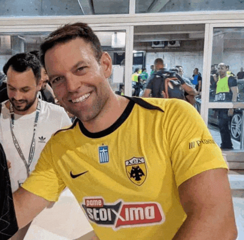 a man wearing a yellow shirt that says aek smiles for the camera
