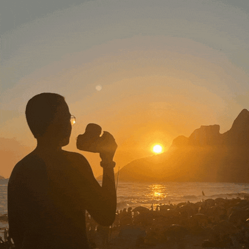 a silhouette of a man holding a camera looking at the sunset over the ocean