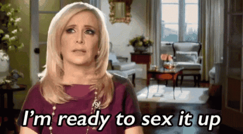 a woman is standing in a living room and saying i 'm ready to sex it up .