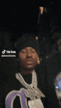 a man wearing a black beanie and a purple shirt with a duke dennis necklace