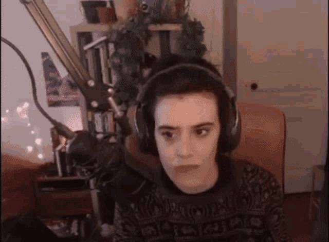 a man wearing headphones and a sweater is sitting in front of a microphone .