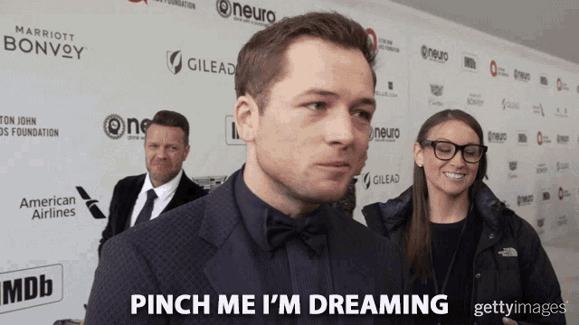 a man in a suit says " pinch me i 'm dreaming " in front of a wall of sponsors
