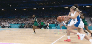 a group of women are playing basketball on a court with a crowd watching .