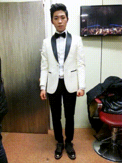 a man in a tuxedo stands in front of a tv